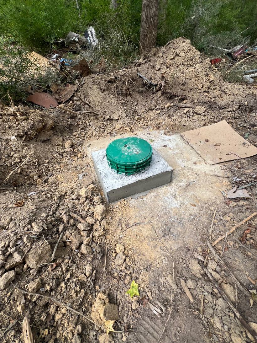 Septic tank riser set on a fresh concrete pad after excavation
